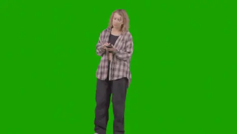 Full Length Studio Shot Of Young Woman Listening To Music On Mobile Phone And Dancing Against Green Screen