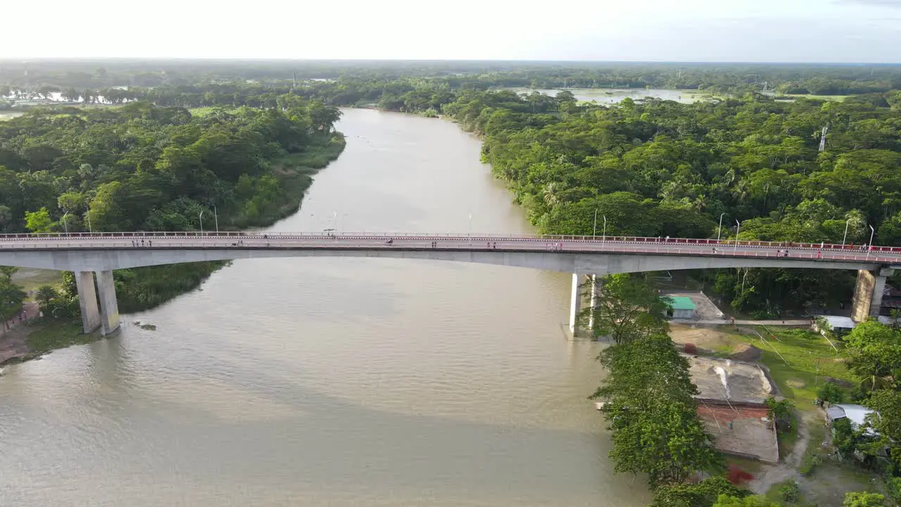 Tracking Aerial shot along Concrete Brigde connecting two Forested riverbanks Bangladesh