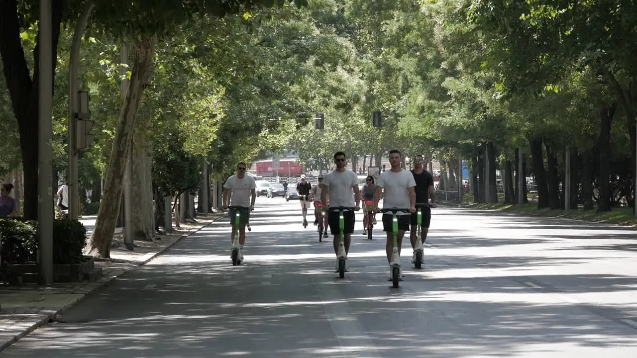 Group of young tourist men riding electric scooters on Madrid city center road Paseo de Recoletos