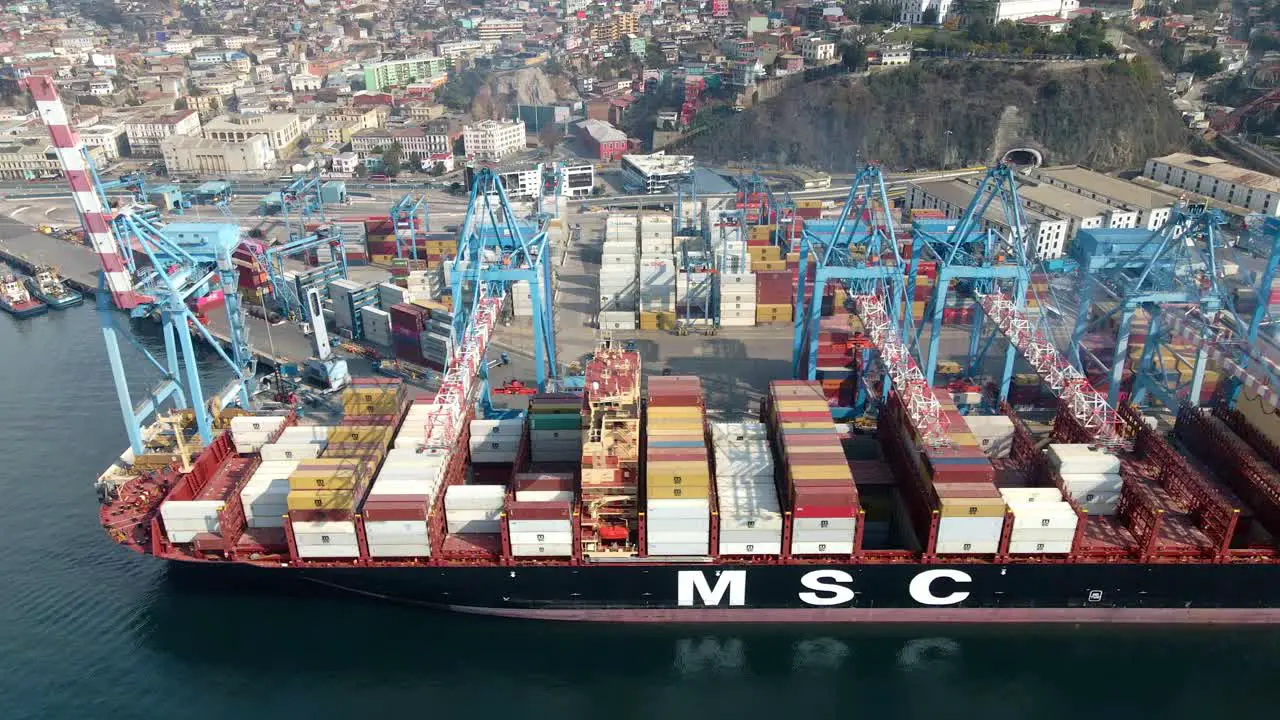 Aerial truck right of a container cargo ship docked near cranes ready to be loaded in Valparaiso Sea Port Chile