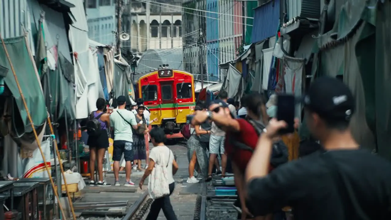 Train arriving at Maeklong Railway Market with people and tourists