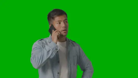 Studio Shot Of Casually Dressed Serious Young Man Talking On Mobile Phone Against Green Screen 