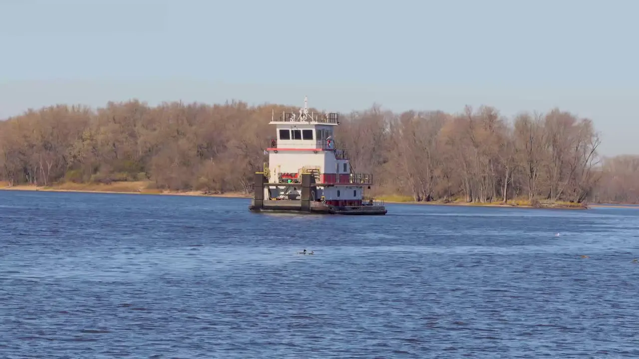 A wide-angle of a barge with no cargo is moving down the Mississippi River