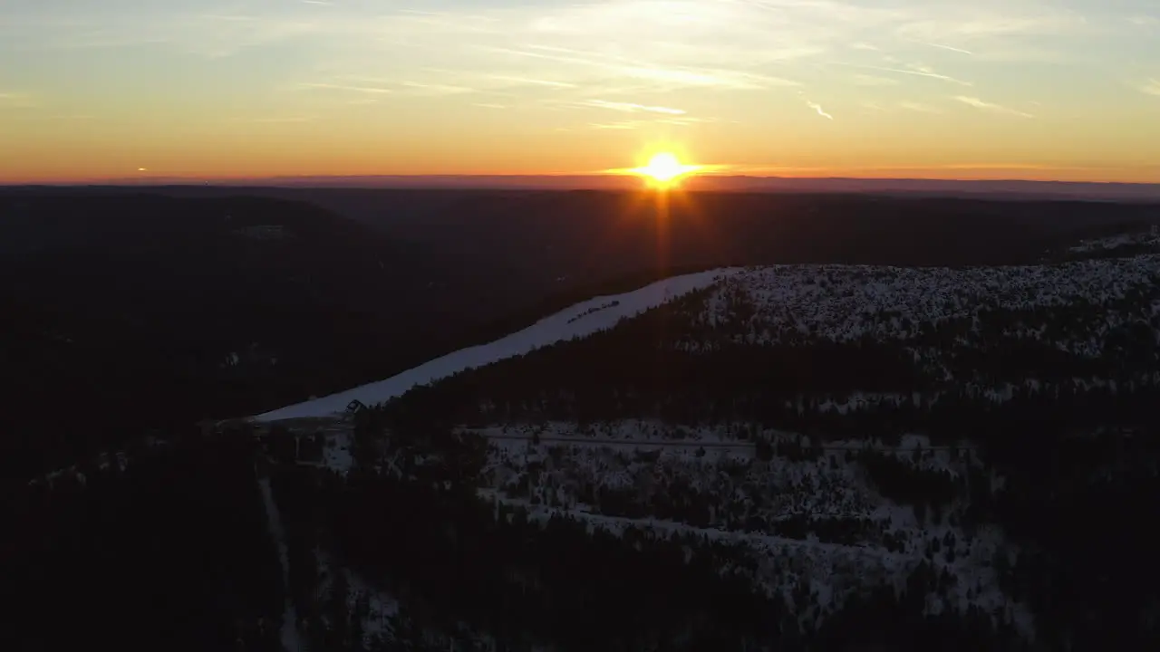 Aerial panning shot over a ski run at sunrise on a snowy black forest mountain top at clear weather