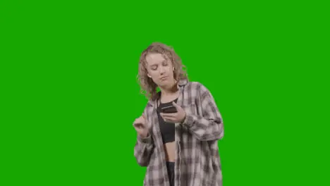 Studio Shot Of Young Woman Listening To Music On Mobile Phone And Dancing Against Green Screen 2