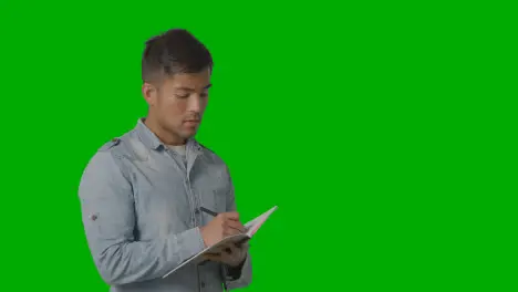 Male University Or College Student Taking Notes In Lecture Or Lesson Against Green Screen 