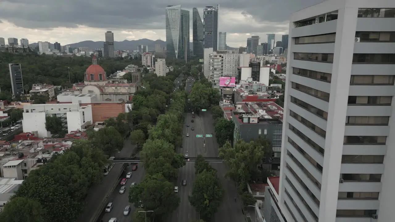 Aerial follows traffic on tree lined street leading in Mexico City