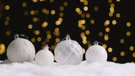 Studio Christmas Still Life With Snow Falling On Decorations With Lights On Background