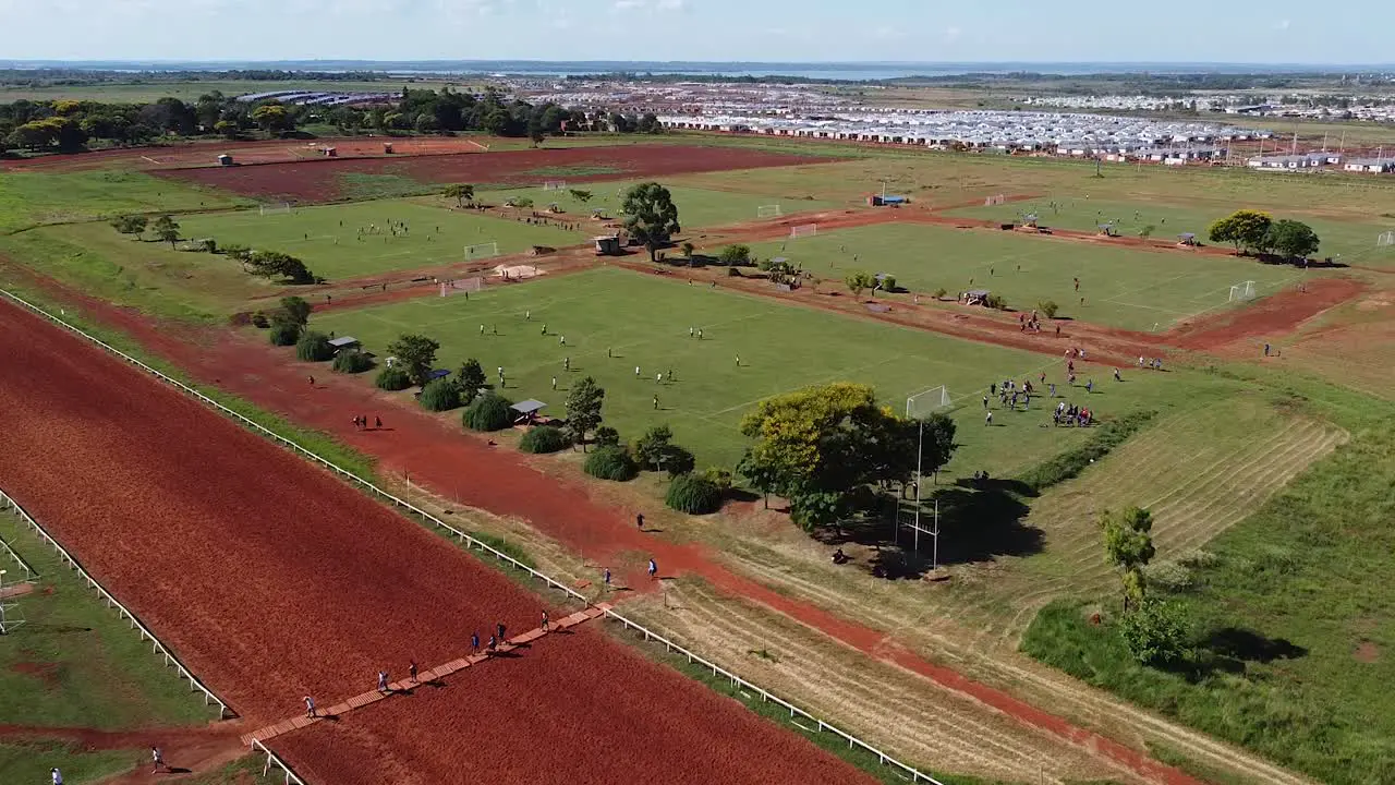 Drone retreat from football matches being played revealing surrounding countryside people walk away from field Posadas hipodrome