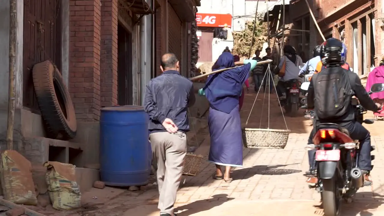 Newari Old woman carries baskets in crowded Bhaktapur street Nepal