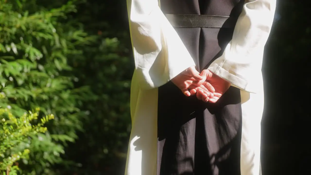 Close up shot of the hands of a monk walking in the forest towards the light