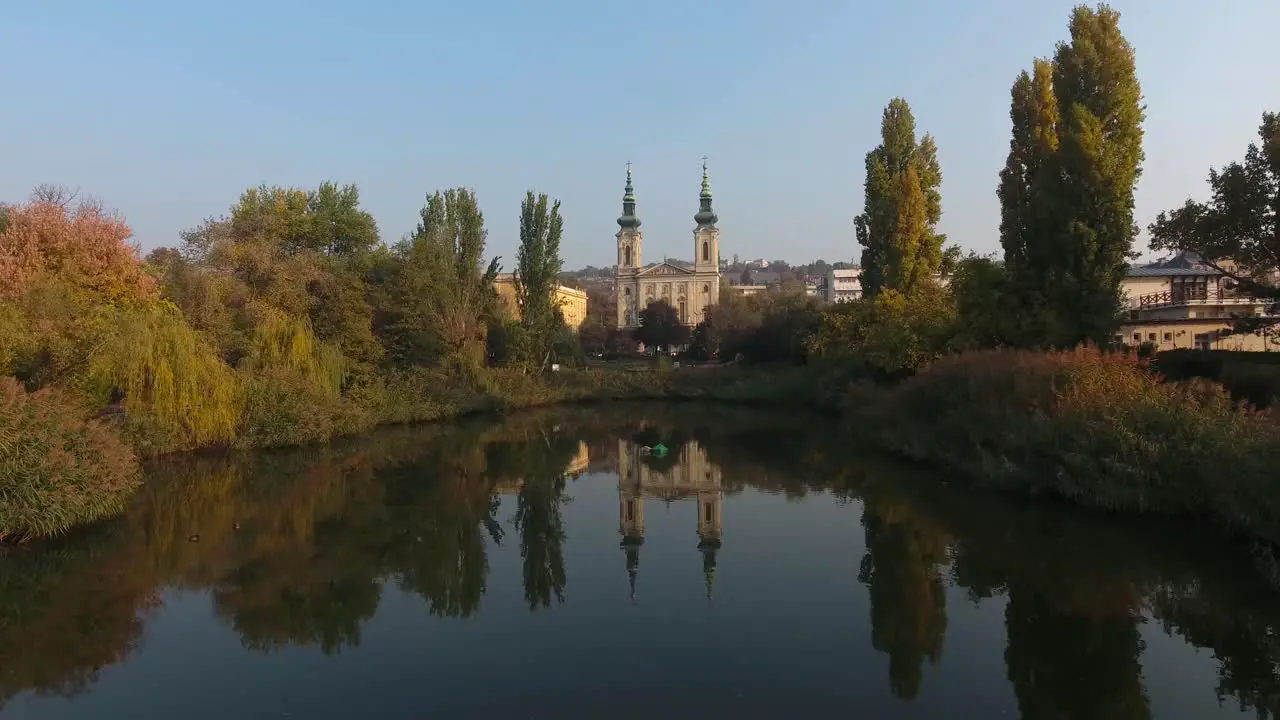 Establishing shot of a chatolic church in a park reflection on the water and traffic in distance