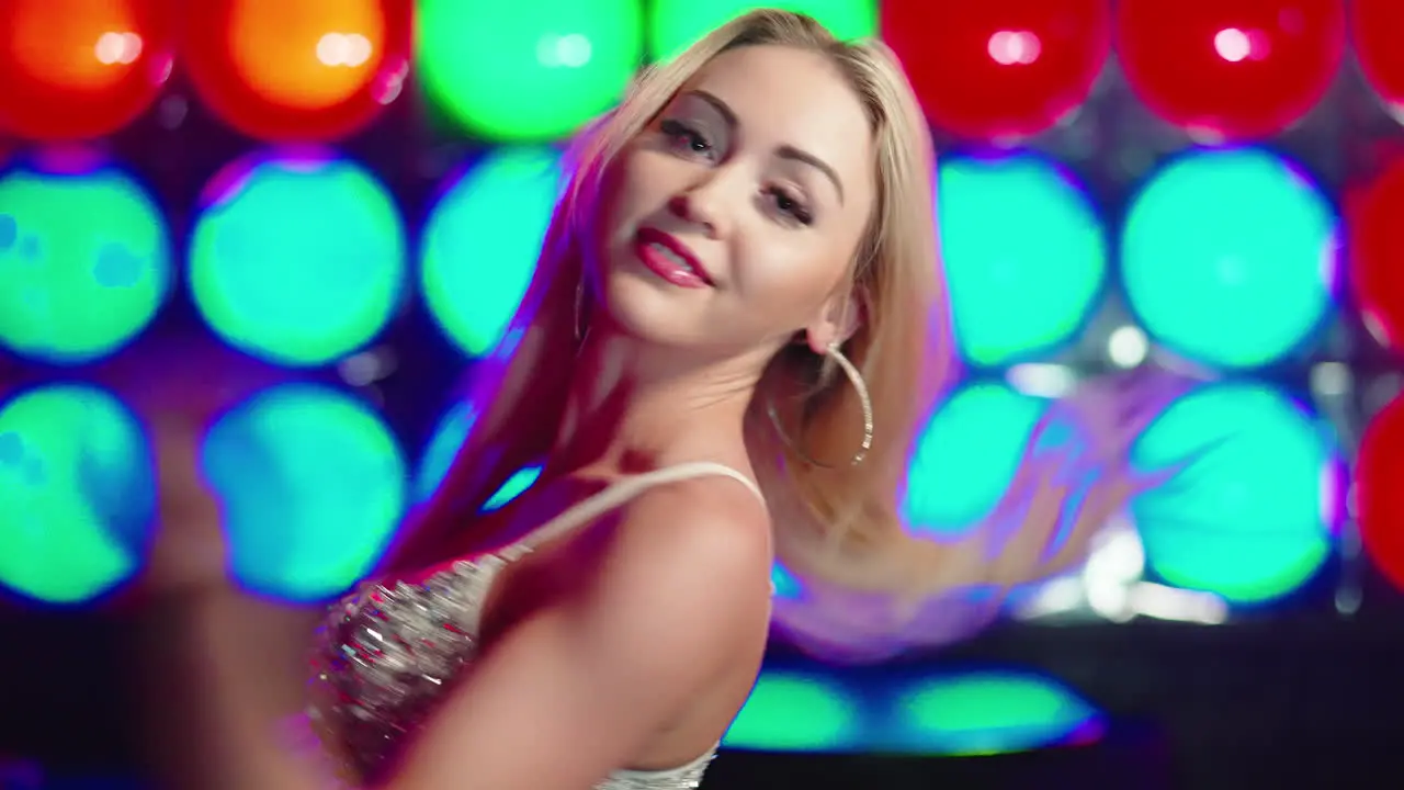 Woman with blonde hair and a sparkly top dancing in a colourful club