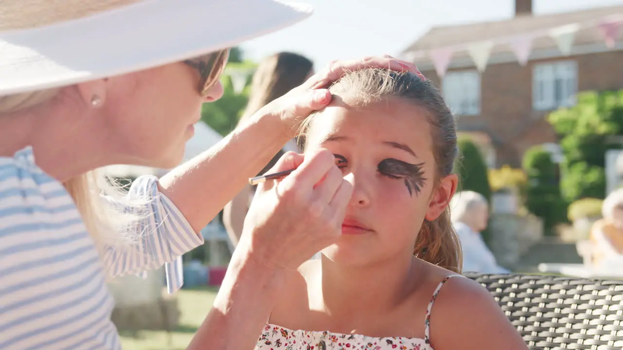 Slow Motion Shot Of Young Girl At Face Painting Stall At Summer Garden Fete