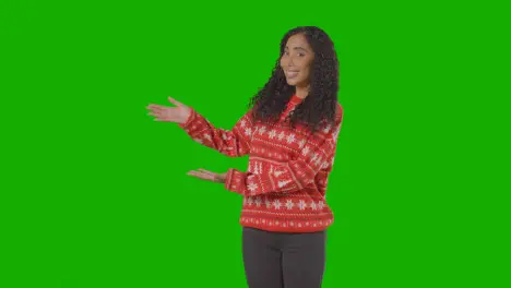 Studio Portrait Of Woman Wearing Christmas Jumper Showing Item Or Object Against Green Screen Smiling At Camera