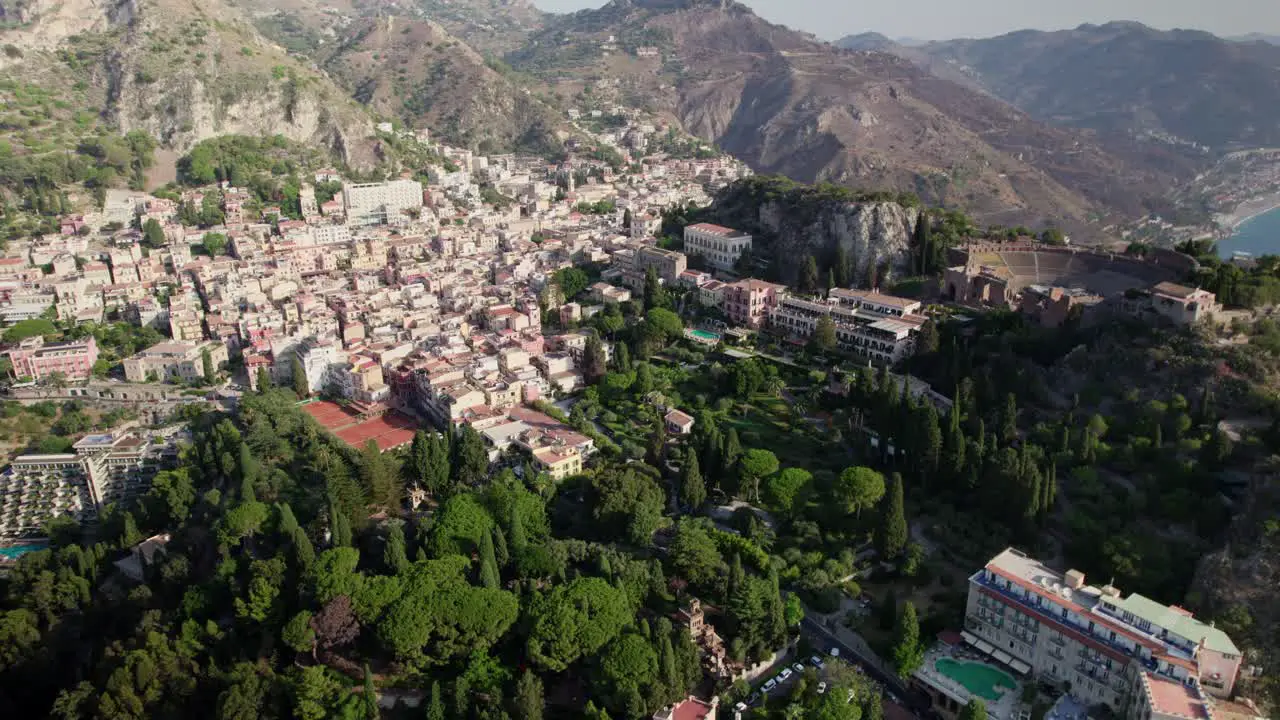 Aerial drone video over Taormina Sicily capturing the old town buildings and green trees and mountains in the background