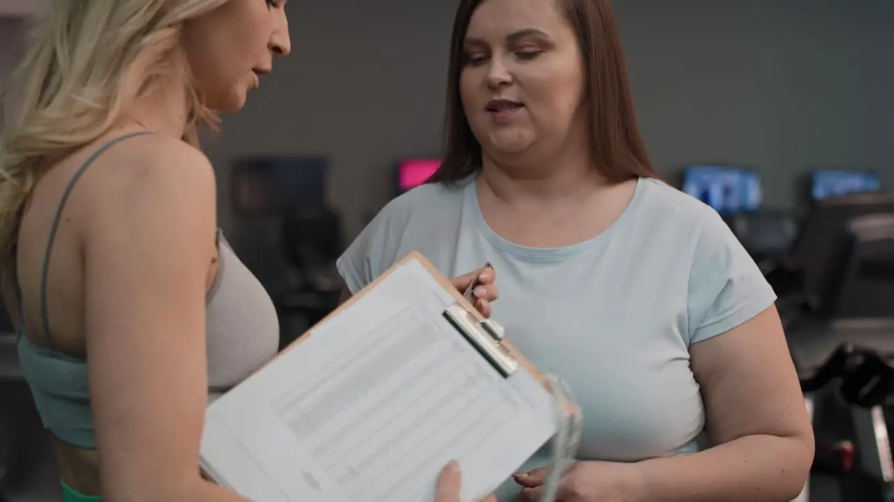 Adult female trainer measuring fat layer of overweight woman with waistline at fitness club