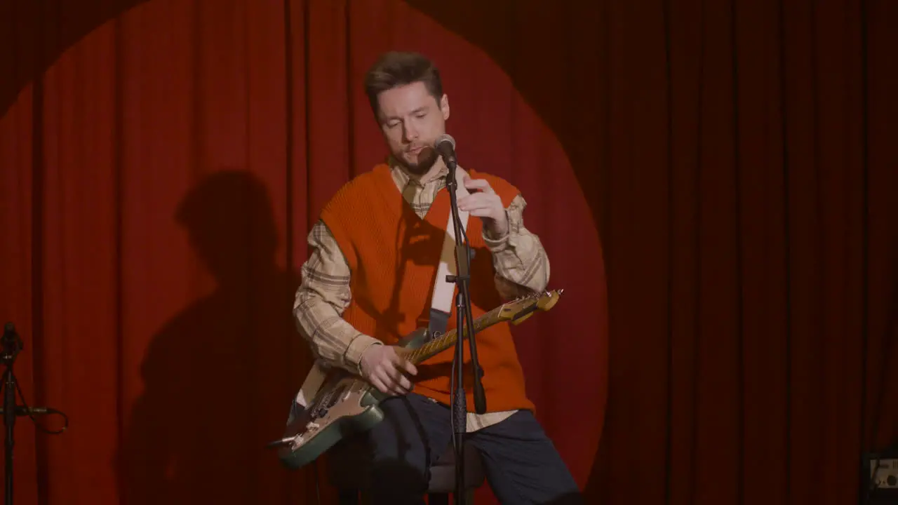 Concentrated Male Musician With Guitar And Microphone Sitting On Stool And Getting Ready For A Live Performance 2