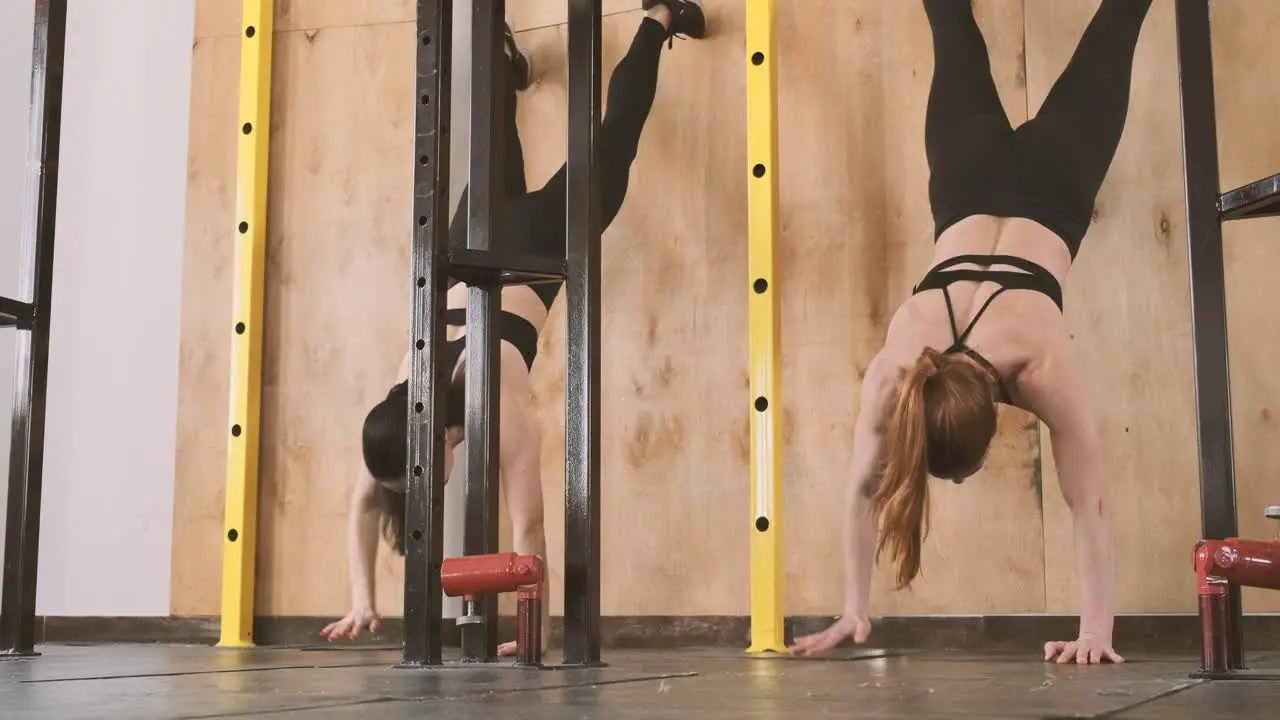 Two Young Athletic Females Doing Abdominal Exercises And Climbing A Wall With Their Feet In The Gym