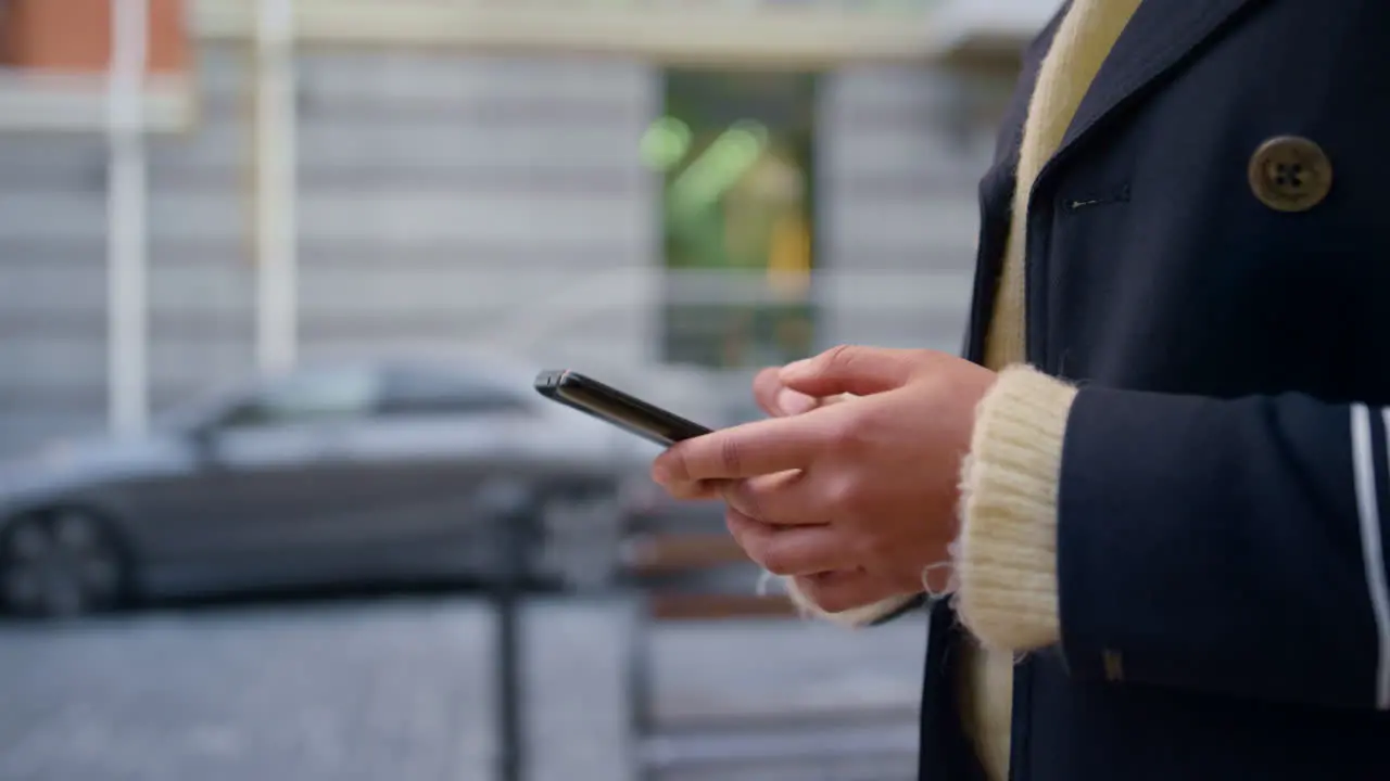 Female hands holding smartphone walking defocused city street alone close up