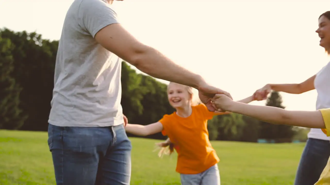 Padres Felices E Hijas Pequeñas Tomándose De La Mano Y Dando Vueltas En El Campo De Hierba Verde En El Parque 2