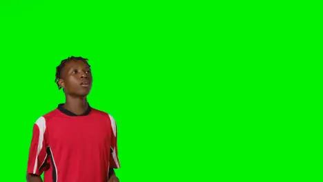 Studio Shot Of Young Male Footballer Wearing Club Kit Controlling Ball With Chest And Passing Against Green Screen