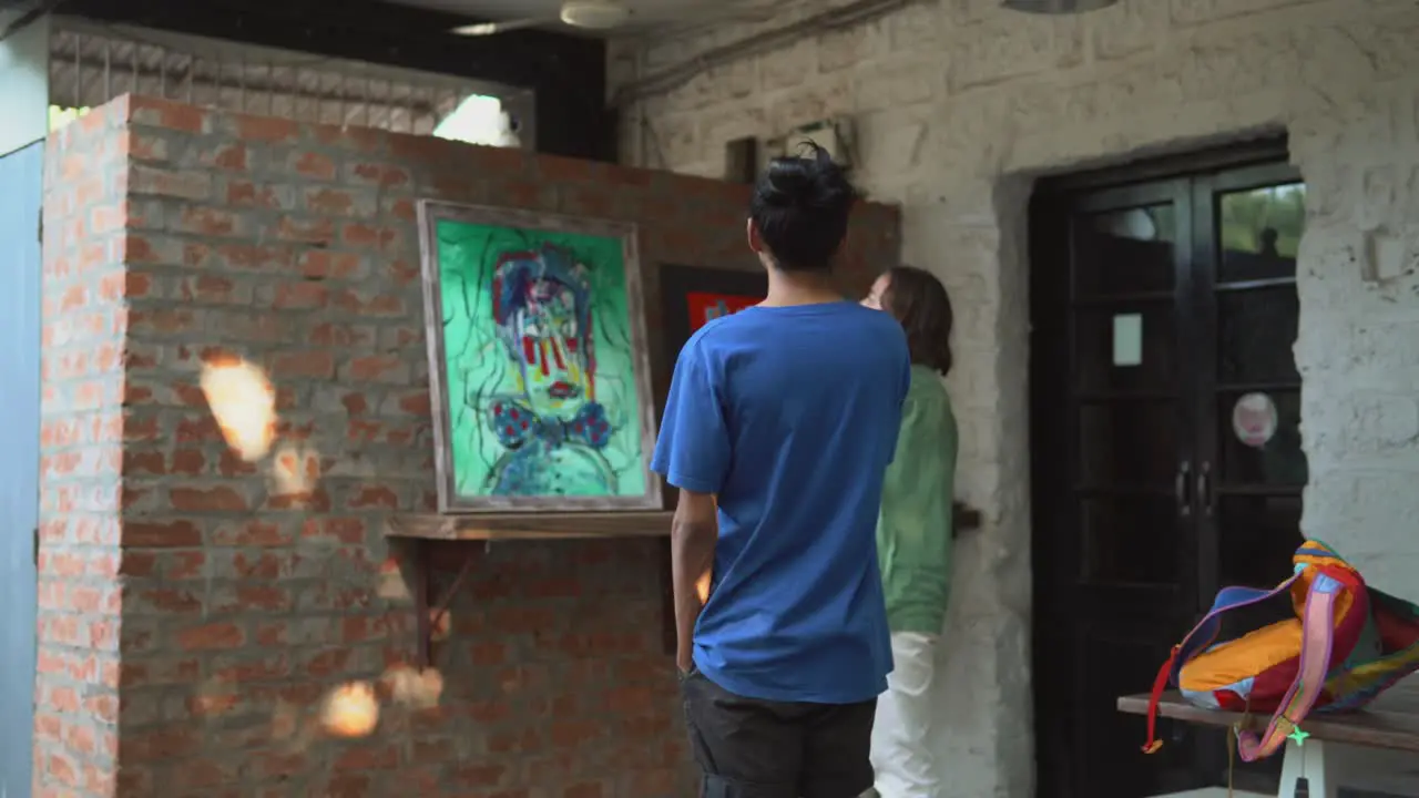 a man in a blue shirt and a man in a green shirt looking at an abstract portrait painting discussing feedback of art