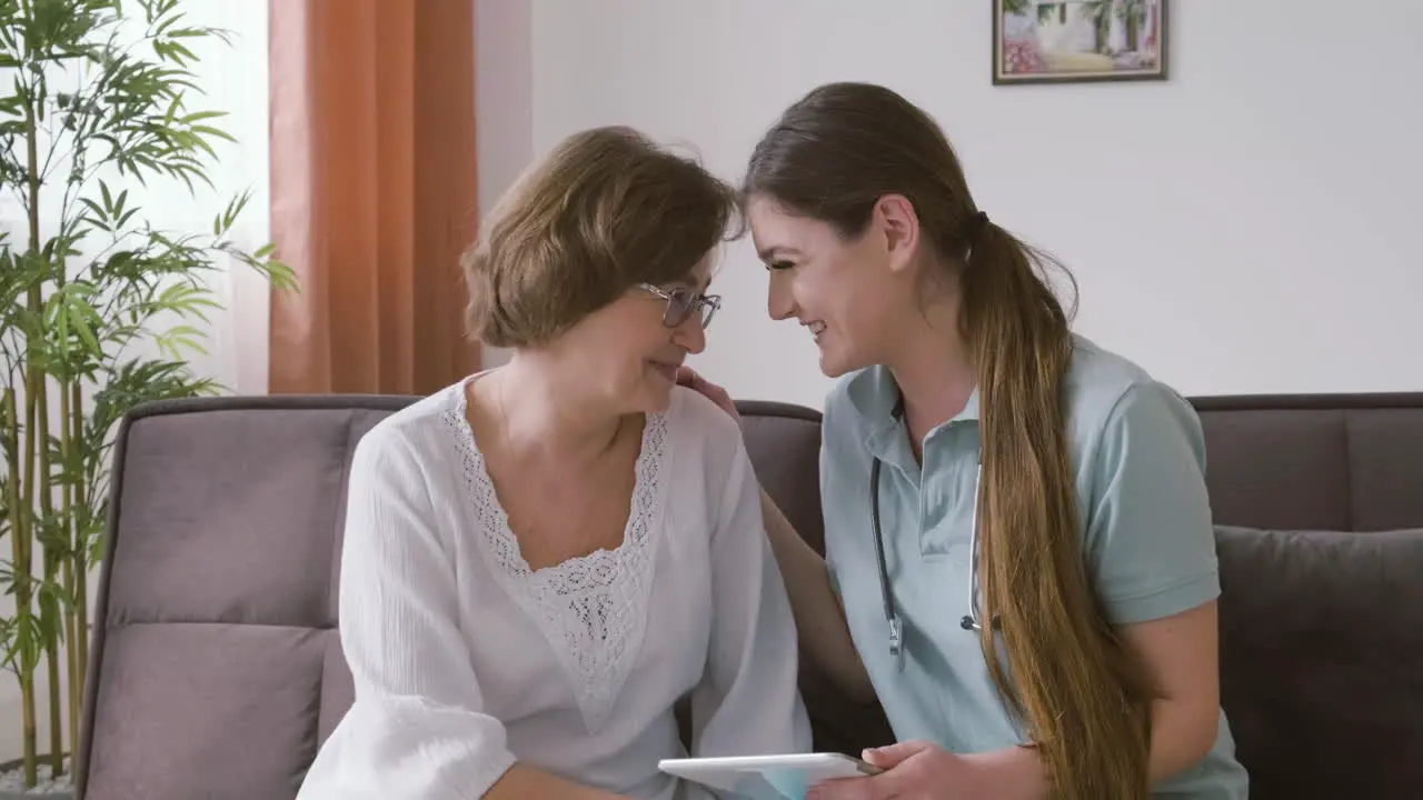 ältere Frau Und Ärztin Sitzen Auf Einem Sofa Und Unterhalten Sich Und Lachen Während Sie Auf Ein Tablet Schauen 1