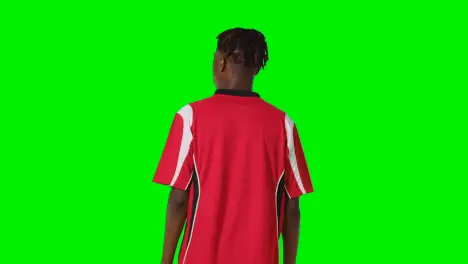 Rear View Of Young Male Footballer Wearing Club Kit Watching Game Against Green Screen