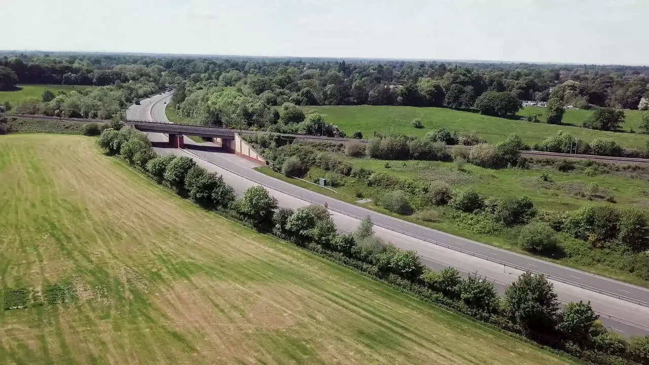 Drone flying over A34 trunk road which is intersected by a railway bridge crossing showing transport cutting through countryside in the UK