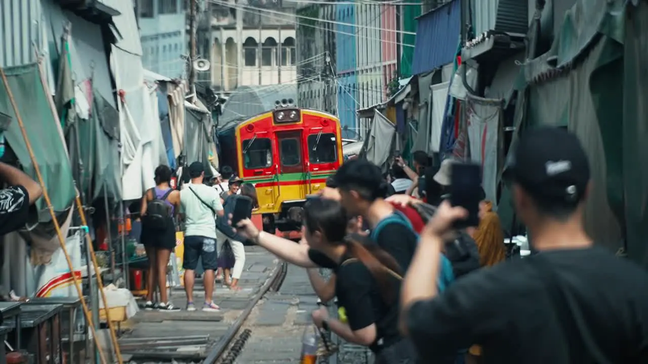 Train travelling in Maeklong Railway Market with tourists on phones