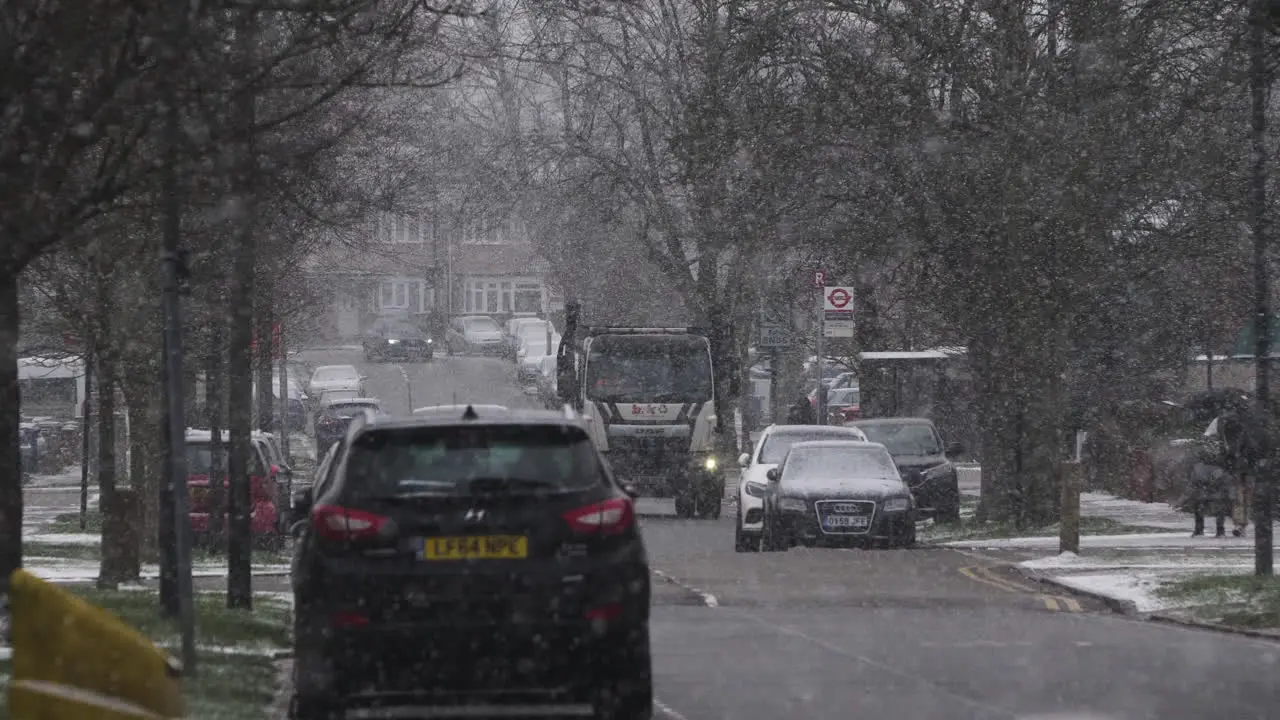 Cars And Skip Lorry Driving Past On Residential Road In Snow