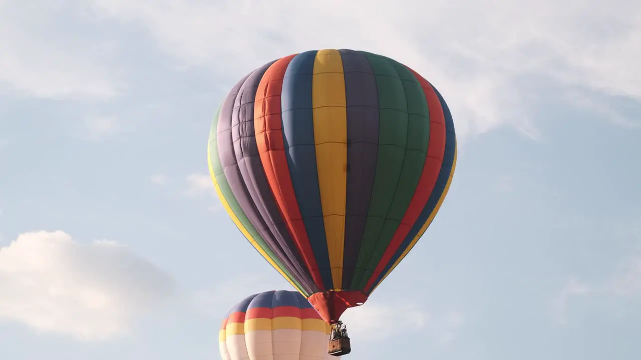 Slow tracking shot of colorful hot air balloons moving past puffy clouds