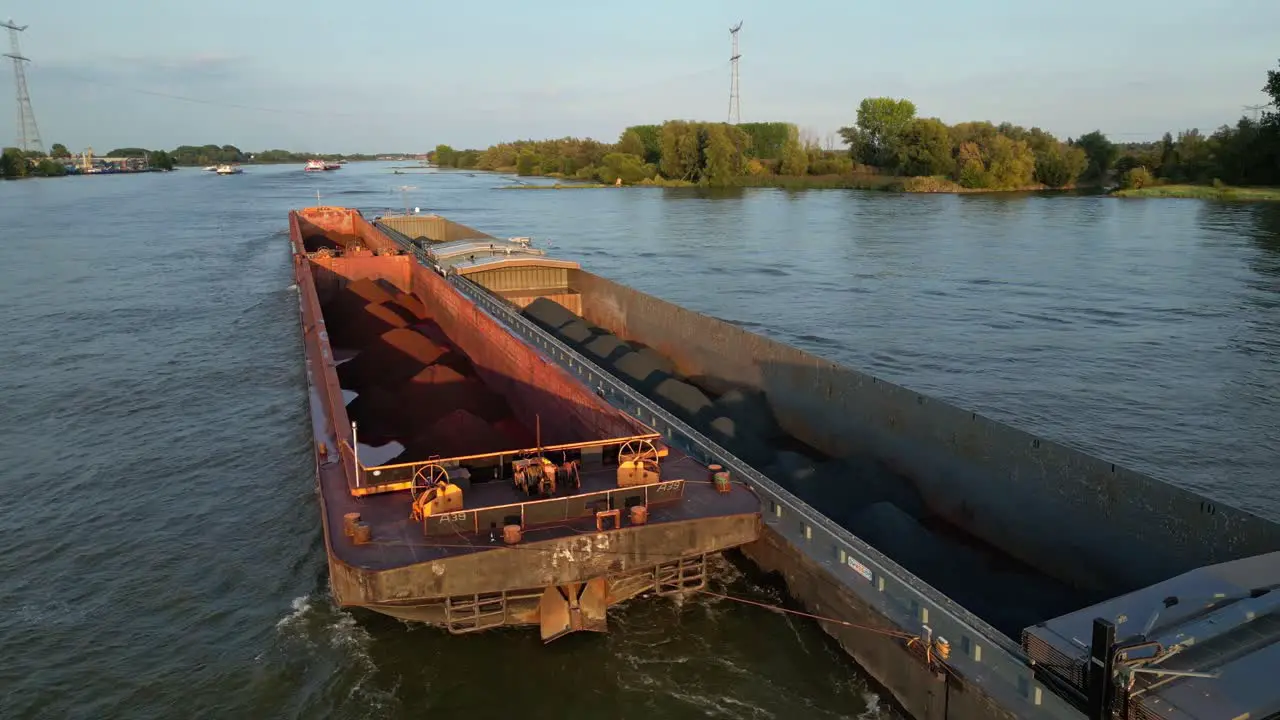 Cargo ship with side attached barge passing on river in golden hour