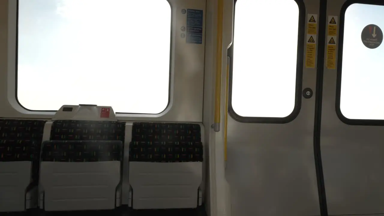 Inside View Of Empty Folded Up Seats On Metropolitan Line Train Carriage With Bright Sunshine And Sun Flares Through Carriage Windows