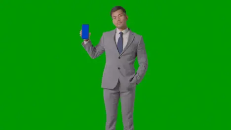 Studio Shot Of Smiling Businessman In Suit Holding Blue Screen Mobile Phone Against Green Screen 2