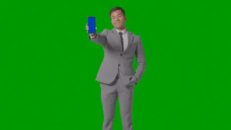 Studio Shot Of Smiling Businessman In Suit Holding Blue Screen Mobile Phone Against Green Screen 1