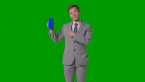 Studio Shot Of Smiling Businessman In Suit Holding Blue Screen Mobile Phone Against Green Screen 3