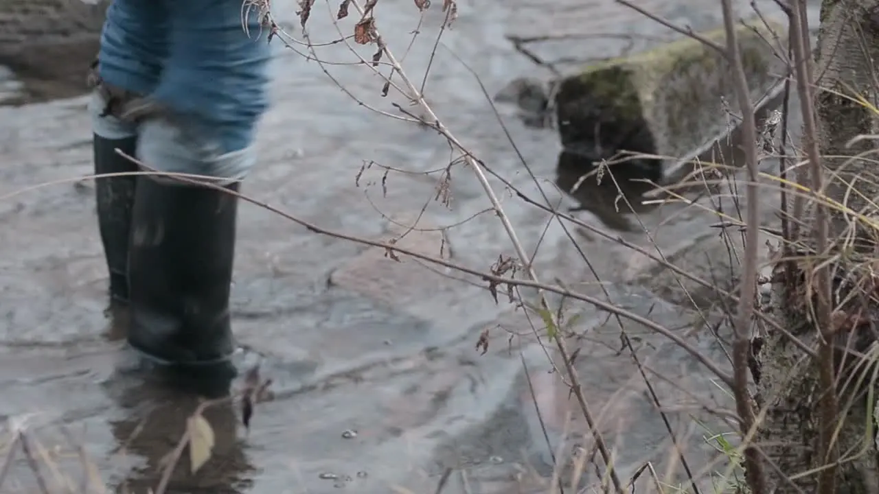 Woman in Wellington boots splashing in stream of water