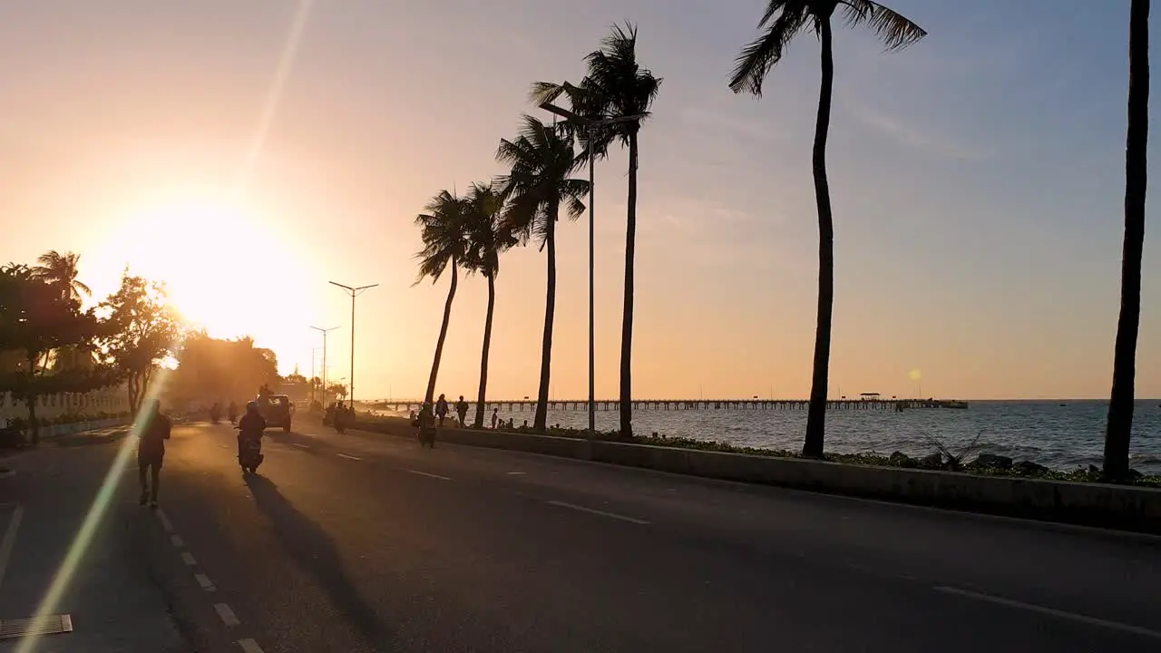 People on the waterfront walking running exercising and commuting traffic and palm trees by the sea during golden sunset in Dili Timor-Leste