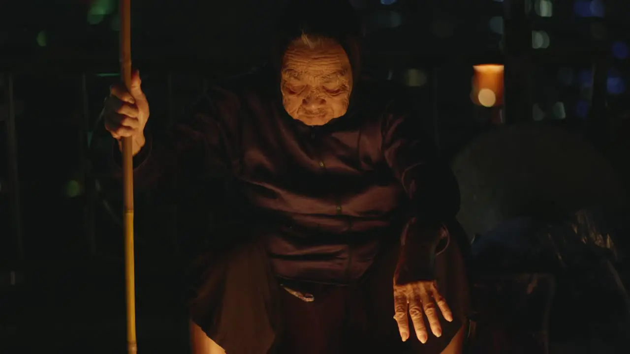 Portrait of old wrinkled Vietnamese woman sitting by river in Hoi An at night