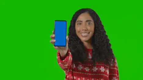 Studio Portrait Of Woman Wearing Christmas Jumper Holding Up Mobile Phone Against Green Screen 2