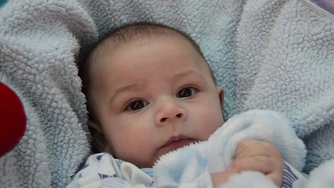 cute tree months old baby boy making funny faces in baby bouncer on light blue blanket