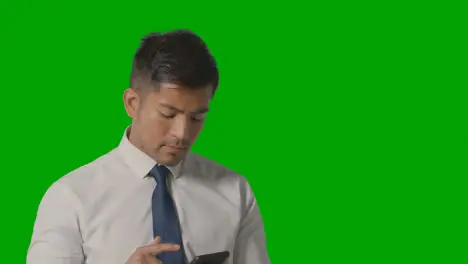 Studio Shot Of Businessman In Shirt And Tie Thinking Using Mobile Phone Against Green Screen 