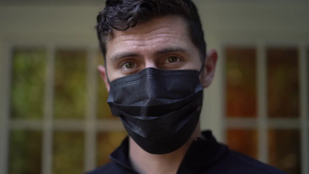 Young man puts on a black face mask to protect himself and others from a virus then looks at the camera 2020 global pandemic