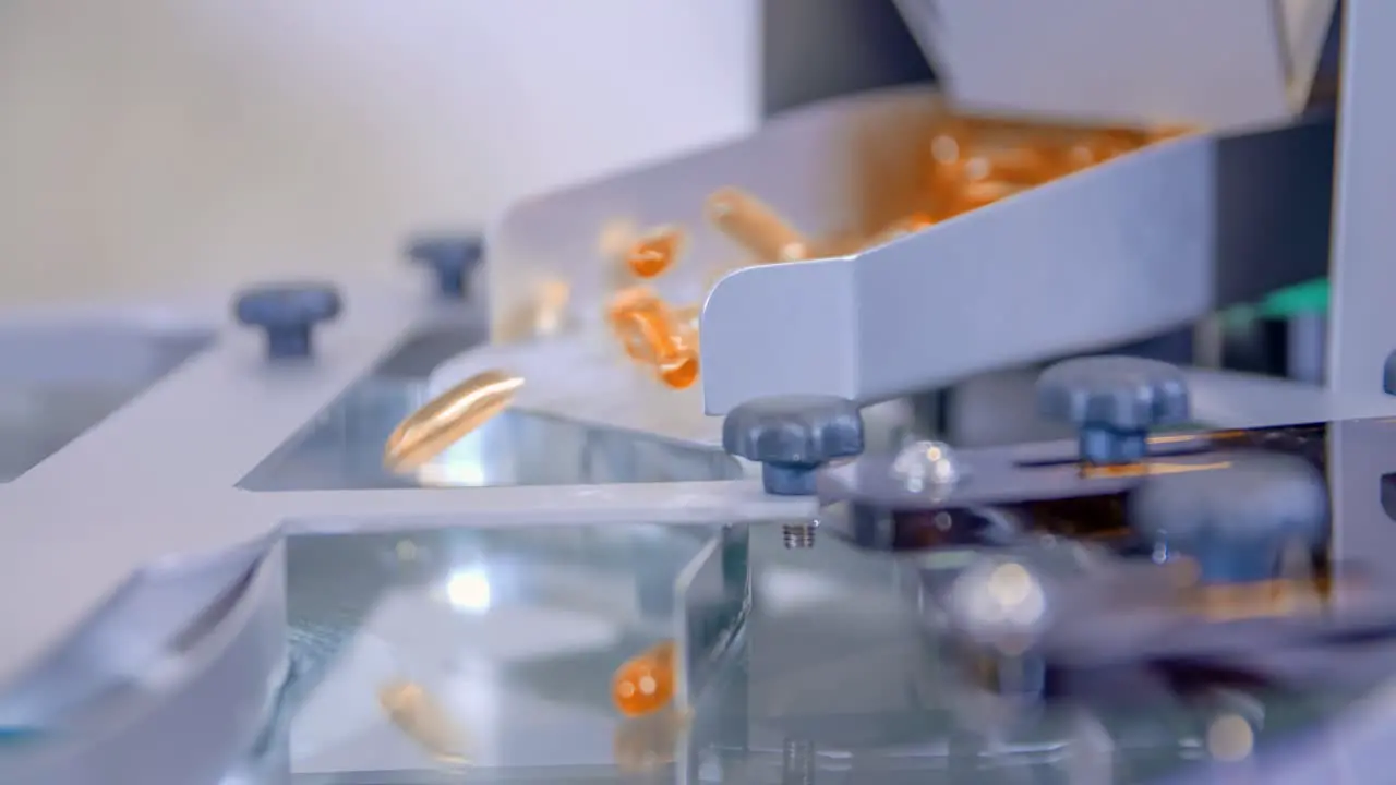 Orange gel capsules falling into a machine in the pharmaceutical lab