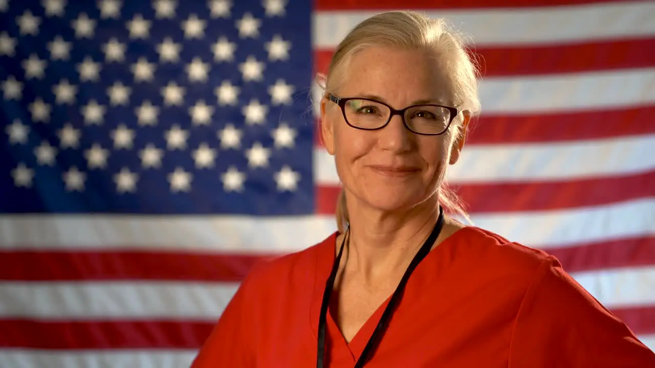 Medium tight portrait of a healthcare nurse turning her head and smiling with out of focus American flag