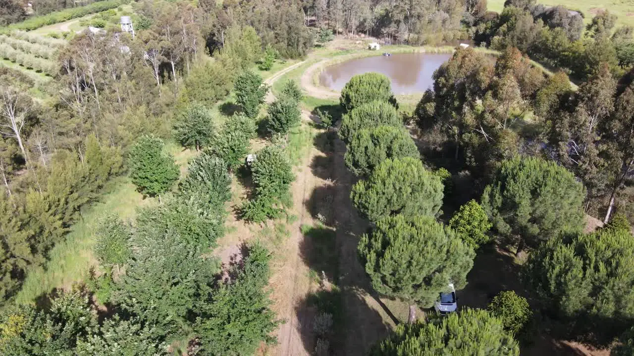 Drone aerial parallax over lush permaculture farm with dam and a campervan