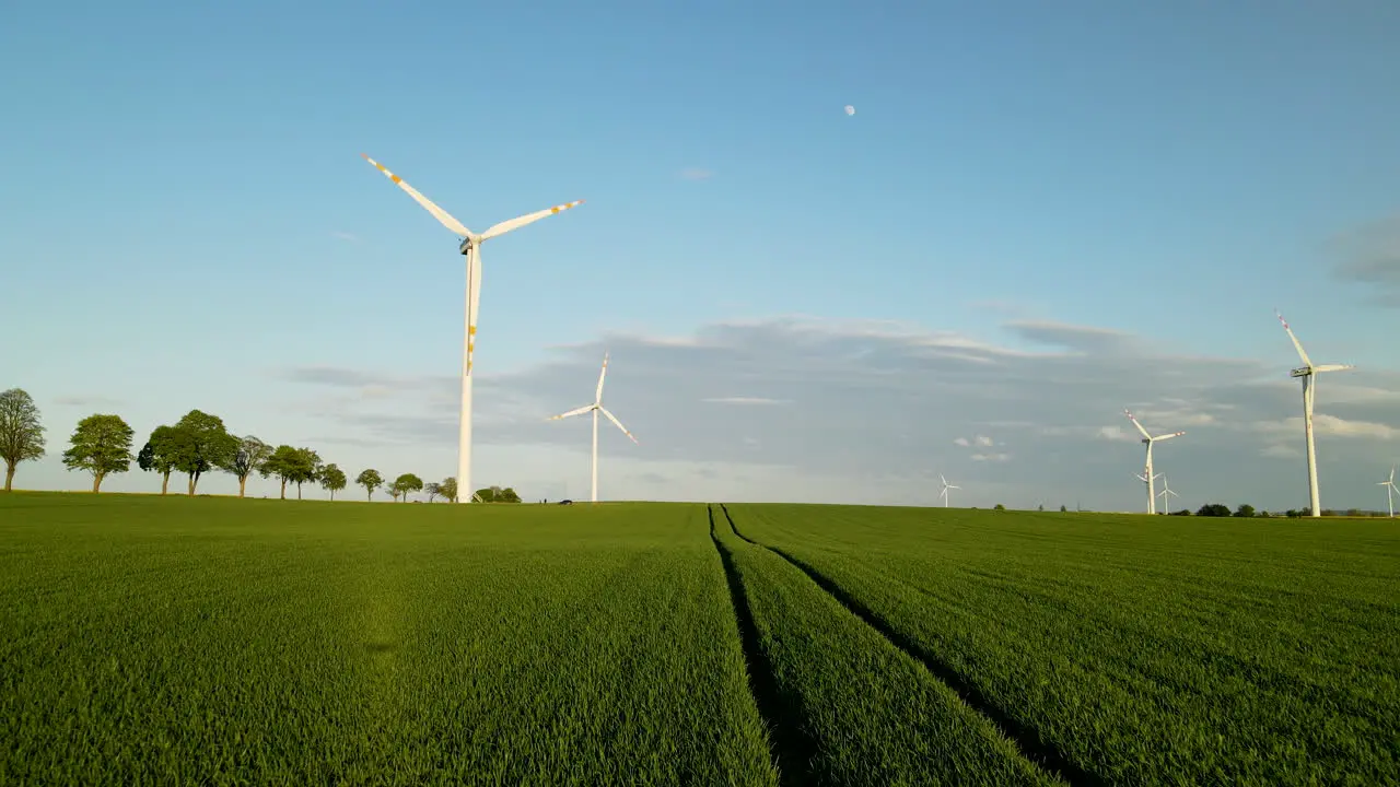 Slow aerial flyover green farm field towards wind turbine farm in the evening