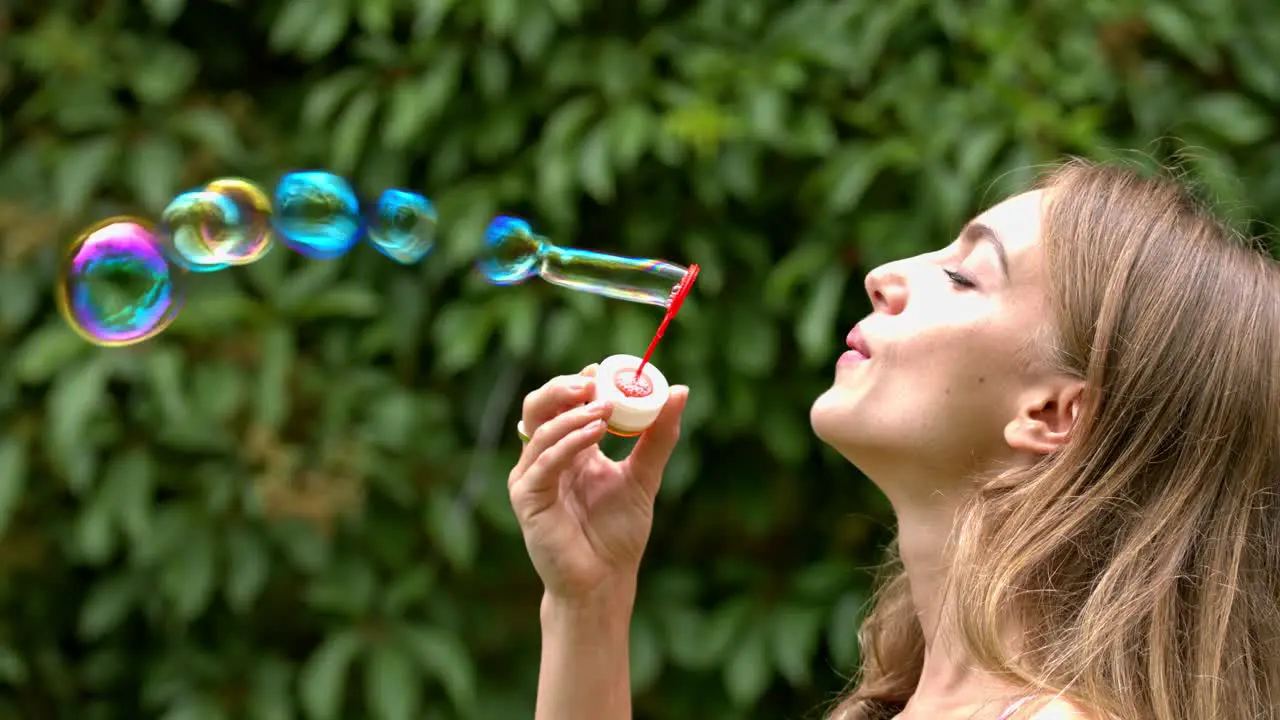 Attractive woman on a summer day in the park is playing by blowing soap bubbles